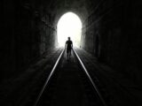 Silhouette eines Menschen auf Bahngleisen in einem dunklen Tunnel vor einem hellen Ausgang